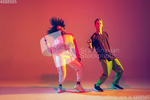 Image of Stylish man and woman dancing hip-hop in bright clothes on gradient background at dance hall in neon light