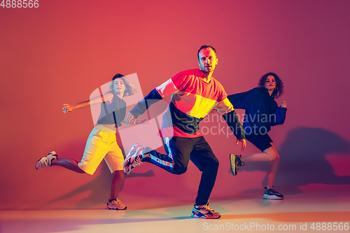 Image of Stylish man and women dancing hip-hop in bright clothes on gradient background at dance hall in neon light