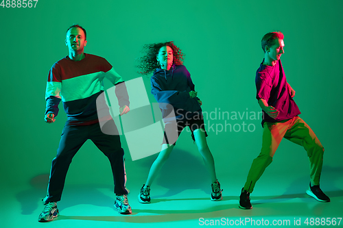 Image of Stylish men and woman dancing hip-hop in bright clothes on gradient background at dance hall in neon light