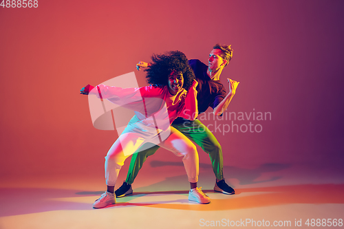 Image of Stylish man and woman dancing hip-hop in bright clothes on gradient background at dance hall in neon light