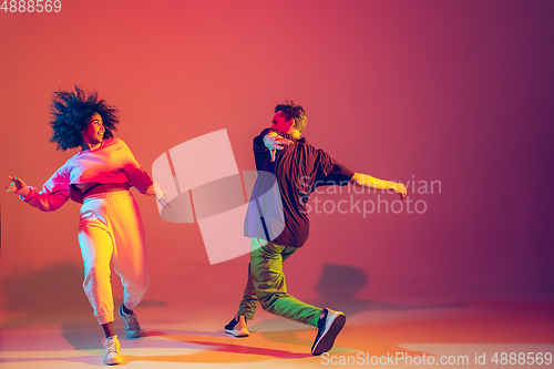 Image of Stylish man and woman dancing hip-hop in bright clothes on gradient background at dance hall in neon light