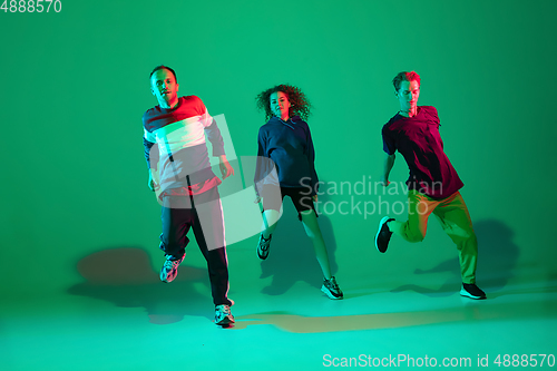 Image of Stylish men and woman dancing hip-hop in bright clothes on gradient background at dance hall in neon light