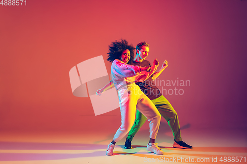 Image of Stylish man and woman dancing hip-hop in bright clothes on gradient background at dance hall in neon light