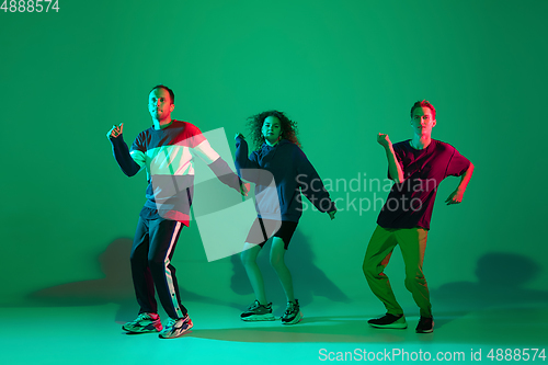 Image of Stylish men and woman dancing hip-hop in bright clothes on gradient background at dance hall in neon light