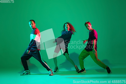 Image of Stylish men and woman dancing hip-hop in bright clothes on gradient background at dance hall in neon light