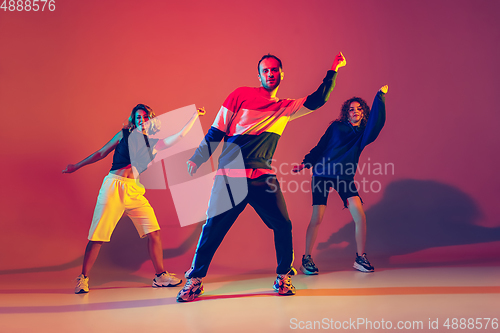 Image of Stylish man and women dancing hip-hop in bright clothes on gradient background at dance hall in neon light