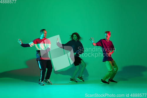 Image of Stylish men and woman dancing hip-hop in bright clothes on gradient background at dance hall in neon light