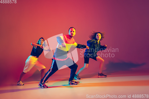 Image of Stylish man and women dancing hip-hop in bright clothes on gradient background at dance hall in neon light