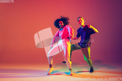 Image of Stylish man and woman dancing hip-hop in bright clothes on gradient background at dance hall in neon light