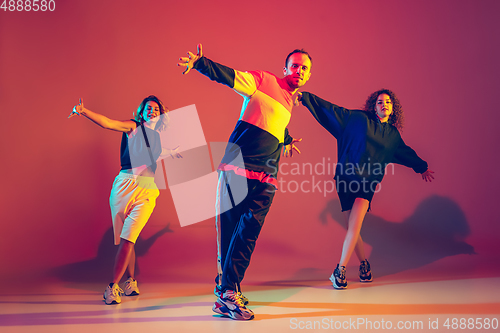 Image of Stylish man and women dancing hip-hop in bright clothes on gradient background at dance hall in neon light