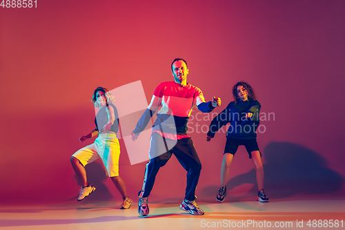 Image of Stylish man and women dancing hip-hop in bright clothes on gradient background at dance hall in neon light