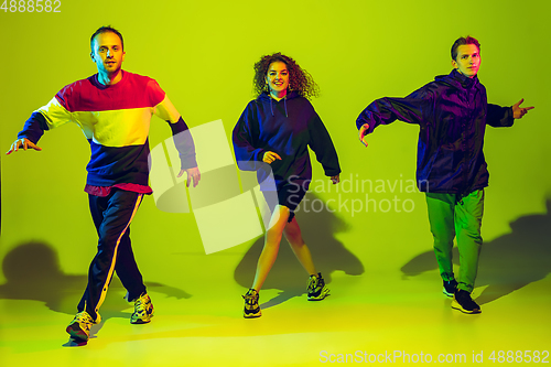 Image of Stylish men and woman dancing hip-hop in bright clothes on gradient background at dance hall in neon light