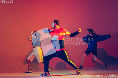 Image of Stylish man and women dancing hip-hop in bright clothes on gradient background at dance hall in neon light