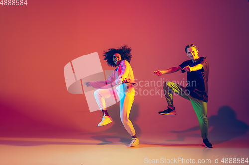 Image of Stylish man and woman dancing hip-hop in bright clothes on gradient background at dance hall in neon light