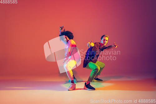 Image of Stylish man and woman dancing hip-hop in bright clothes on gradient background at dance hall in neon light