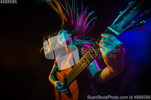 Image of Playing guitar. Young woman with smoke and neon light on black background. Highly tensioned, wide angle, fish eye view