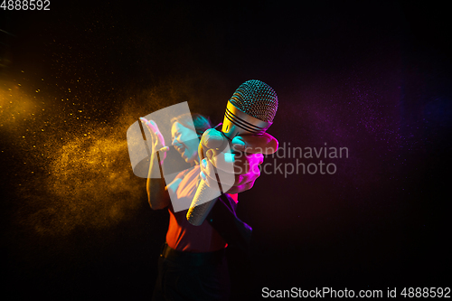 Image of Singing with microphone. Young woman with smoke and neon light on black background. Highly tensioned, wide angle, fish eye view