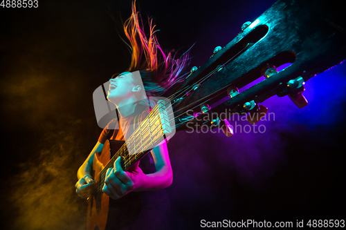 Image of Playing guitar. Young woman with smoke and neon light on black background. Highly tensioned, wide angle, fish eye view