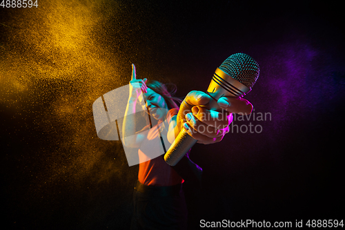 Image of Singing with microphone. Young woman with smoke and neon light on black background. Highly tensioned, wide angle, fish eye view