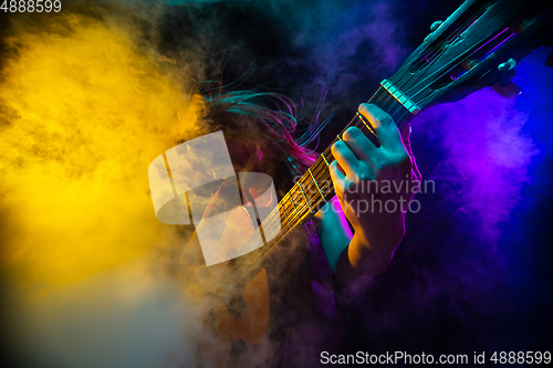 Image of Playing guitar. Young woman with smoke and neon light on black background. Highly tensioned, wide angle, fish eye view