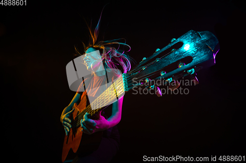 Image of Playing guitar. Young woman with smoke and neon light on black background. Highly tensioned, wide angle, fish eye view