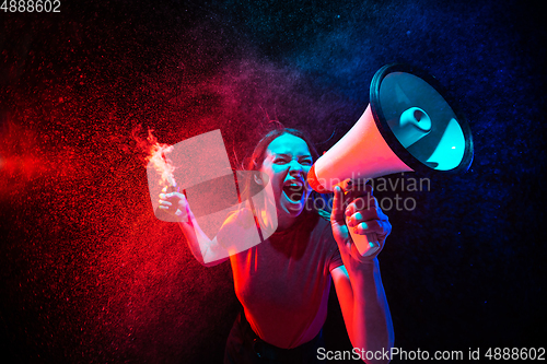 Image of Shouting with megaphone. Young woman with smoke and neon light on black background. Highly tensioned, wide angle, fish eye view