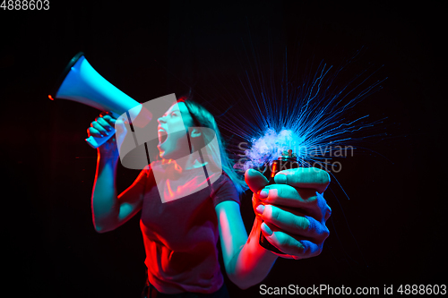 Image of Shouting with megaphone. Young woman with smoke and neon light on black background. Highly tensioned, wide angle, fish eye view