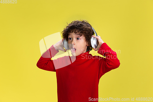 Image of Pretty young curly boy in red wear on yellow studio background. Childhood, expression, fun.