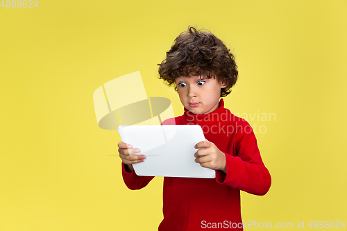 Image of Pretty young curly boy in red wear on yellow studio background. Childhood, expression, fun.