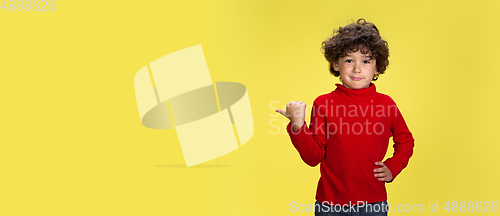 Image of Pretty young curly boy in red wear on yellow studio background. Childhood, expression, fun.