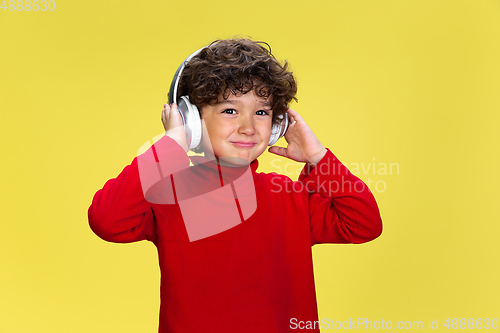 Image of Pretty young curly boy in red wear on yellow studio background. Childhood, expression, fun.