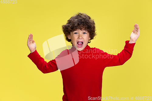 Image of Pretty young curly boy in red wear on yellow studio background. Childhood, expression, fun.