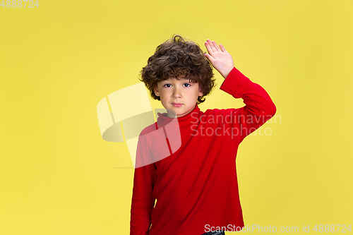 Image of Pretty young curly boy in red wear on yellow studio background. Childhood, expression, fun.