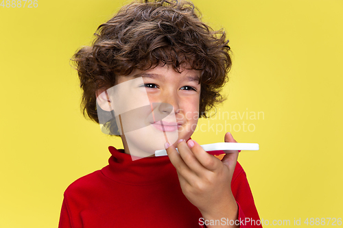 Image of Pretty young curly boy in red wear on yellow studio background. Childhood, expression, fun.