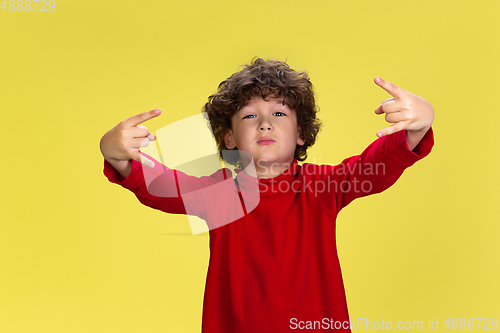 Image of Pretty young curly boy in red wear on yellow studio background. Childhood, expression, fun.