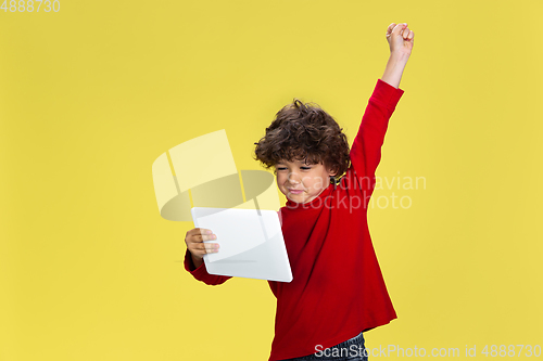 Image of Pretty young curly boy in red wear on yellow studio background. Childhood, expression, fun.