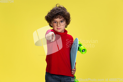 Image of Pretty young curly boy in red wear on yellow studio background. Childhood, expression, fun.