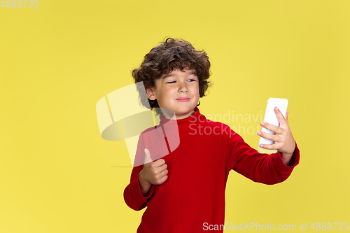 Image of Pretty young curly boy in red wear on yellow studio background. Childhood, expression, fun.