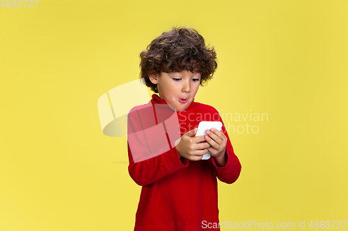 Image of Pretty young curly boy in red wear on yellow studio background. Childhood, expression, fun.