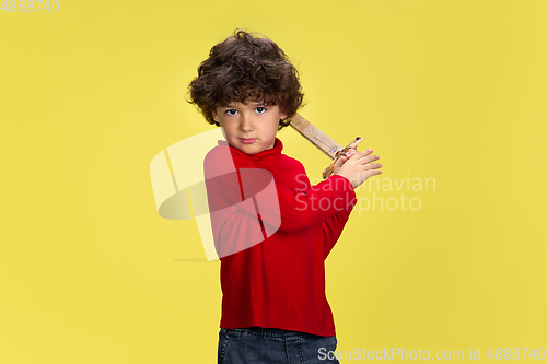 Image of Pretty young curly boy in red wear on yellow studio background. Childhood, expression, fun.