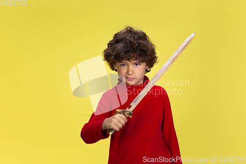 Image of Pretty young curly boy in red wear on yellow studio background. Childhood, expression, fun.