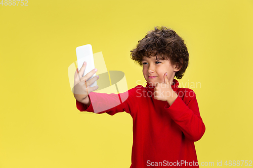 Image of Pretty young curly boy in red wear on yellow studio background. Childhood, expression, fun.