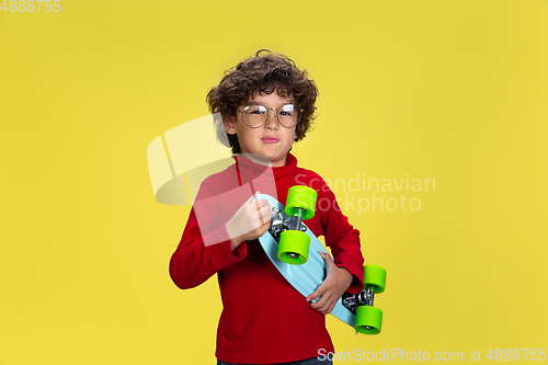 Image of Pretty young curly boy in red wear on yellow studio background. Childhood, expression, fun.