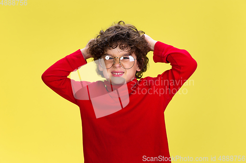 Image of Pretty young curly boy in red wear on yellow studio background. Childhood, expression, fun.