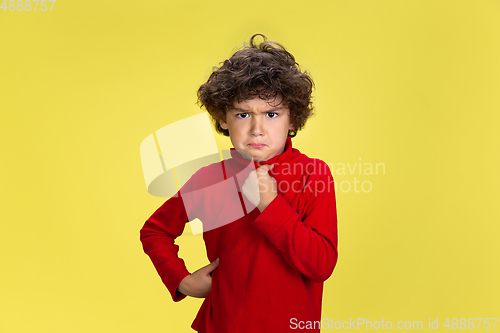 Image of Pretty young curly boy in red wear on yellow studio background. Childhood, expression, fun.