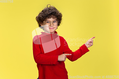 Image of Pretty young curly boy in red wear on yellow studio background. Childhood, expression, fun.