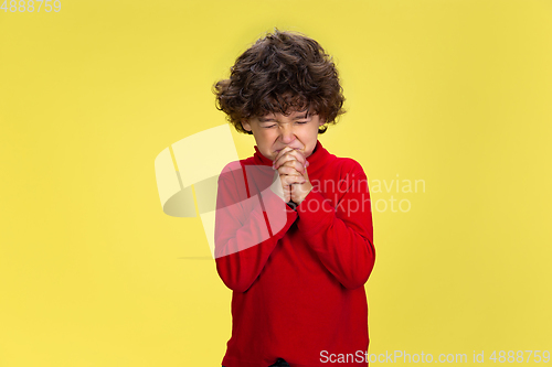 Image of Pretty young curly boy in red wear on yellow studio background. Childhood, expression, fun.
