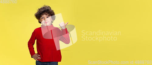 Image of Pretty young curly boy in red wear on yellow studio background. Childhood, expression, fun.