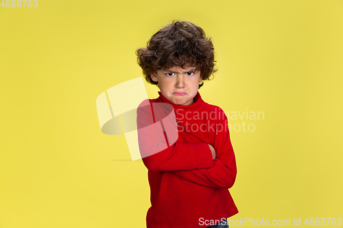 Image of Pretty young curly boy in red wear on yellow studio background. Childhood, expression, fun.