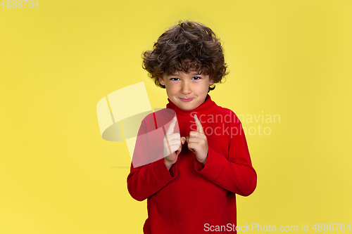 Image of Pretty young curly boy in red wear on yellow studio background. Childhood, expression, fun.